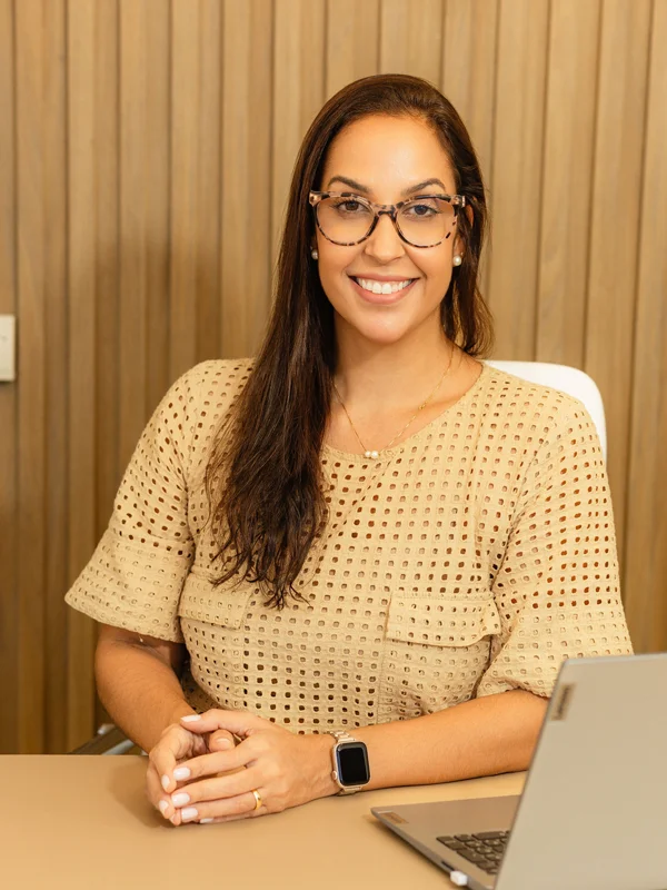 Dra. Fernanda Telles sorrindo, sentada à mesa em seu consultório